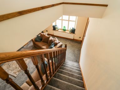 A staircase with wooden banister leading to a living room with a carpet and a sofa with cushions at The Anvil in Broughton-In-Furness
