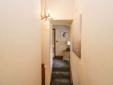 A hallway with carpeted stairs leading to a small table with a lamp and framed artwork at The Anvil in Broughton-In-Furness