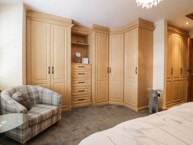 A bedroom with wooden wardrobes a plaid armchair a round glass side table and a decorative dog figure at The Anvil in Broughton-In-Furness