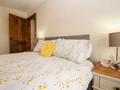 A bedroom with a bed covered in floral bedding and a yellow cushion with bedside tables and lamps at The Anvil in Broughton-In-Furness