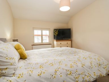 A bedroom with a bed a window and a chest of drawers with a television and flowers at The Anvil in Broughton-In-Furness