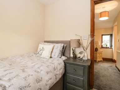A bedroom with a bed beside a bedside table and a view into a hallway with a chest of drawers at The Anvil in Broughton-In-Furness