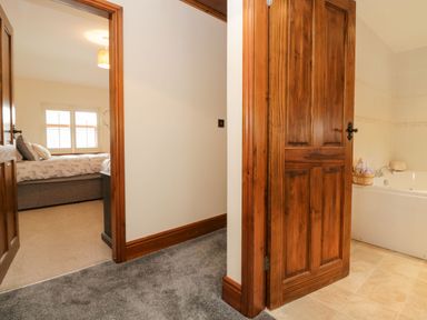 A hallway with two open wooden doors showing a bedroom with a bed and a bathroom with a bathtub at The Anvil in Broughton-In-Furness