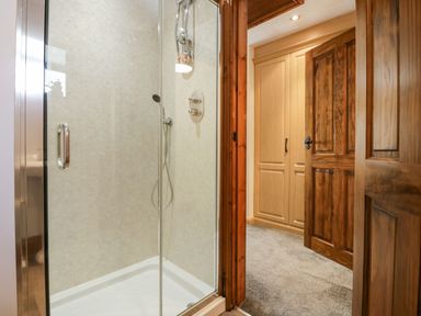 A bathroom with a glass shower enclosure next to a wooden door leading to a carpeted room with a wooden wardrobe at The Anvil in Broughton-In-Furness