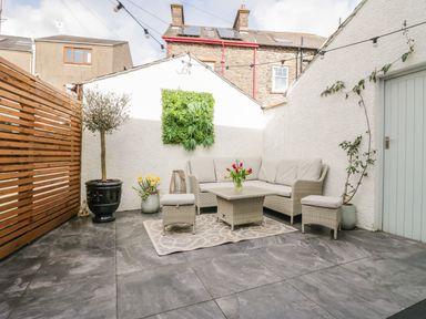 An outdoor patio with a sectional sofa sofa table two stools potted plants and string lights at The Anvil in Broughton-In-Furness