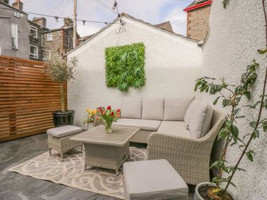 An outdoor patio with rattan furniture and plants on a patterned rug at The Anvil in Broughton-In-Furness
