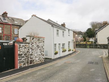 A street view of a white house with flower boxes on windows and a stone wall on the side at The Anvil in Broughton-In-Furness