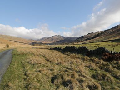 A country road with grass and stone fences beside hills under a blue sky at The Anvil in Broughton-In-Furness
