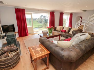 A living room with brown leather sofas a wooden coffee table flowers in a vase red curtains a wood stove and a basket of firewood at Whiteadder Bank in Berwick-Upon-Tweed