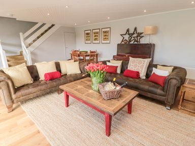 A living room with two brown sofas around a wooden coffee table with flowers and bottles at Whiteadder Bank in Berwick-Upon-Tweed