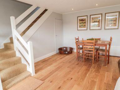 A dining area with wooden table and chairs next to a staircase and a pet bed at Whiteadder Bank in Berwick-Upon-Tweed