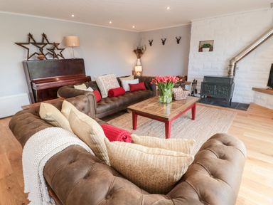 A living room with brown sofas a wooden coffee table with flowers a piano and a wood stove at Whiteadder Bank in Berwick-Upon-Tweed