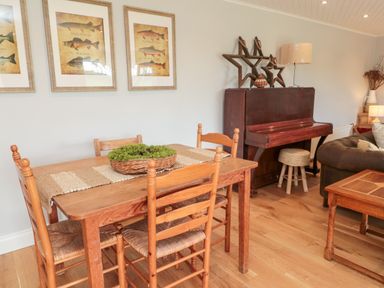 A dining area with wooden table and chairs next to a piano and decorative wall art at Whiteadder Bank in Berwick-Upon-Tweed