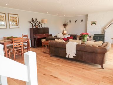 A living room with brown leather sofas a wooden dining table a piano and a stove at Whiteadder Bank in Berwick-Upon-Tweed