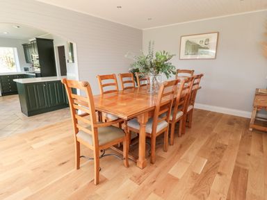 A dining room with a wooden table and eight chairs and a vase with greenery on the table at Whiteadder Bank in Berwick-Upon-Tweed