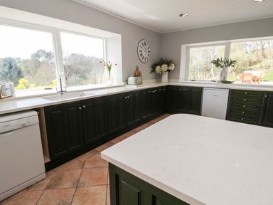 A kitchen with black cabinets white countertops a dishwasher flowers clock and large windows at Whiteadder Bank in Berwick-Upon-Tweed