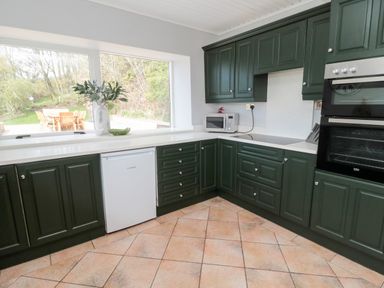 A kitchen with green cabinets a white countertop a microwave a built in oven and a window showing an outdoor table at Whiteadder Bank in Berwick-Upon-Tweed