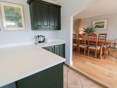 A kitchen with green cabinets and white countertops connected to a dining room with wooden table and chairs at Whiteadder Bank in Berwick-Upon-Tweed