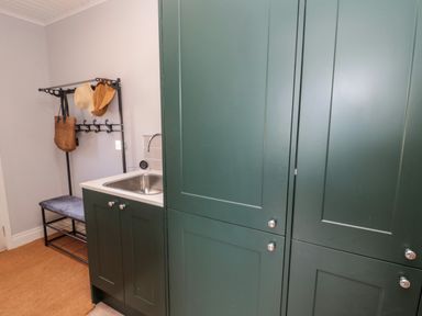 A utility room with dark green cabinets a small sink and a metal coat rack with hats and a bag at Whiteadder Bank in Berwick-Upon-Tweed
