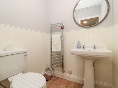 A bathroom with a toilet, pedestal sink, towel radiator with towel, round mirror, and a small trash bin at Whiteadder Bank in Berwick-Upon-Tweed