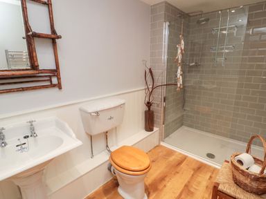A bathroom with a sink a toilet with a wooden seat a glass shower enclosure and a basket with toilet paper at Whiteadder Bank in Berwick-Upon-Tweed