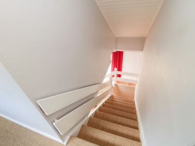 A staircase with carpeted steps and white wooden railing leading to a room with red curtains at Whiteadder Bank in Berwick-Upon-Tweed