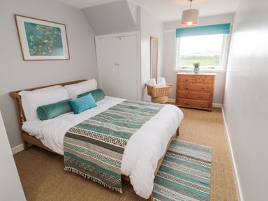 A bedroom with a bed covered in white sheets and teal patterned blankets a wooden dresser under a window and a wicker basket with towels at Whiteadder Bank in Berwick-Upon-Tweed