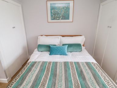 A bedroom with a double bed white pillows teal decorative cushions and a patterned blanket at Whiteadder Bank in Berwick-Upon-Tweed
