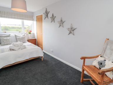 A bedroom with a bed with pillows and towels near a window and a wooden chair with cushions at Whiteadder Bank in Berwick-Upon-Tweed