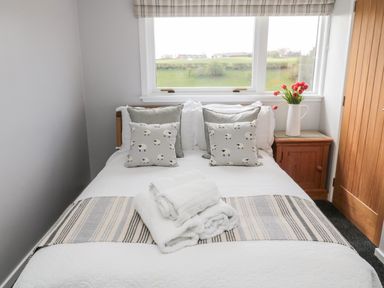 A bedroom with a bed with cushions and towels next to a window and a wooden nightstand with flowers at Whiteadder Bank in Berwick-Upon-Tweed