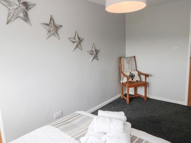 A bedroom corner with a wooden chair holding cushions a bed with folded towels and star-shaped wall decorations at Whiteadder Bank in Berwick-Upon-Tweed