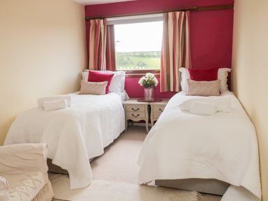 A bedroom with two single beds with white bedding and red pillows with a window and nightstand in between at Whiteadder Bank in Berwick-Upon-Tweed