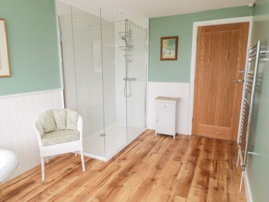 A bathroom with a glass shower enclosure a white chair a wooden door a small white cabinet and a towel rack at Whiteadder Bank in Berwick-Upon-Tweed