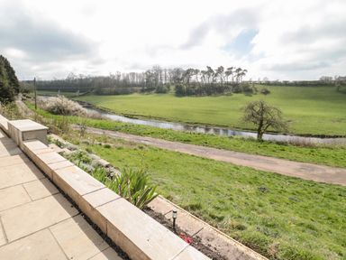 A patio overlooking a river and a grassy field with trees at Whiteadder Bank in Berwick-Upon-Tweed