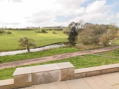 A paved patio with a stone bench overlooking a dirt path river and grassy fields at Whiteadder Bank in Berwick-Upon-Tweed
