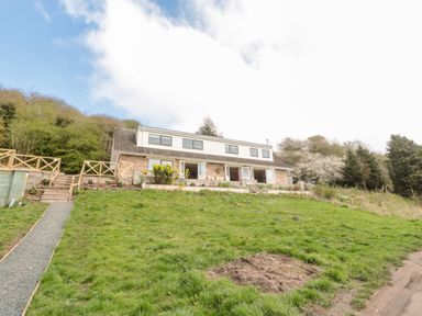 A two-story house with a sloped roof and multiple windows surrounded by a grassy lawn and trees at Whiteadder Bank in Berwick-Upon-Tweed