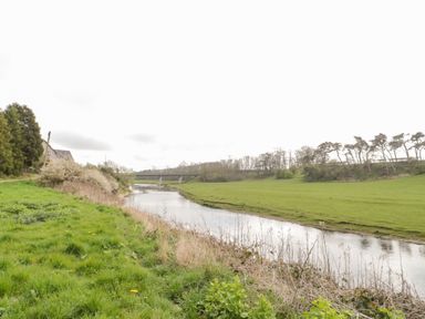 A river flowing through a grassy landscape with trees and a bridge at Whiteadder Bank in Berwick-Upon-Tweed