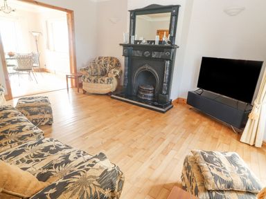 A living room with patterned sofas a black fireplace a television and a wooden floor at Cloughoge House Kilrush County Clare