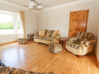 A living room with a patterned sofa armchair wooden door and window at Cloughoge House in Kilrush County Clare