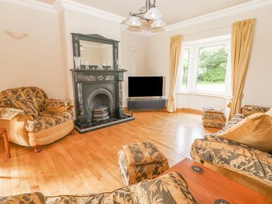 A living room with patterned armchairs a black fireplace a television and a window with curtains at Cloughoge House in Kilrush County Clare