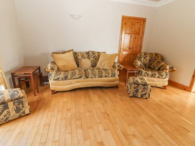 A living room with patterned sofa and armchair wooden floor wooden door and side tables at Cloughoge House in Kilrush County Clare