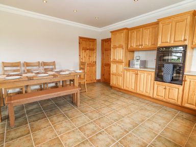 A kitchen with wooden cabinets a dining table with chairs and bench at Cloughoge House Kilrush County Clare