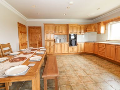 A kitchen with wooden cabinets a dining table set with plates and a bench at Cloughoge House in Kilrush County Clare