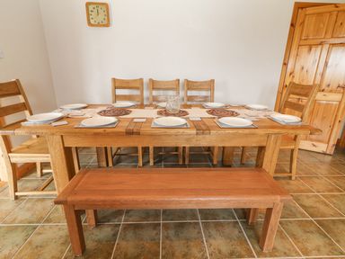 A dining room with a wooden table set with plates wooden chairs a bench and a wall clock at Cloughoge House in Kilrush County Clare