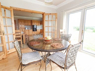 A dining area with a round table and four chairs next to sliding glass doors and an open doorway to a kitchen at Cloughoge House Kilrush County Clare