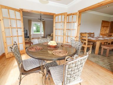 A dining area with a round table and chairs next to a wooden dining table set behind wooden folding glass doors at Cloughoge House Kilrush County Clare