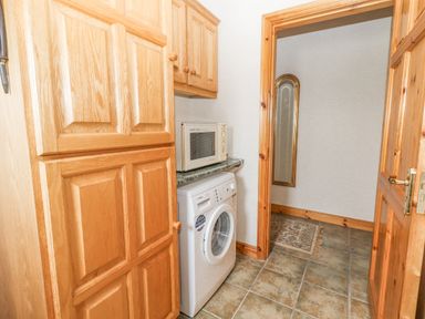 A laundry room with a washing machine countertop microwave wooden cabinets and a floor mirror at Cloughoge House Kilrush County Clare