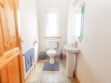 A bathroom with a toilet a sink a mirror a window a towel on a radiator and a wooden door at Cloughoge House in Kilrush County Clare