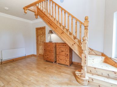 An empty room with wooden staircase two wooden dressers a table lamp and a wooden door at Cloughoge House in Kilrush County Clare