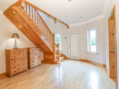 An entryway with wooden staircase wooden dressers and a side table lamp at Cloughoge House in Kilrush County Clare